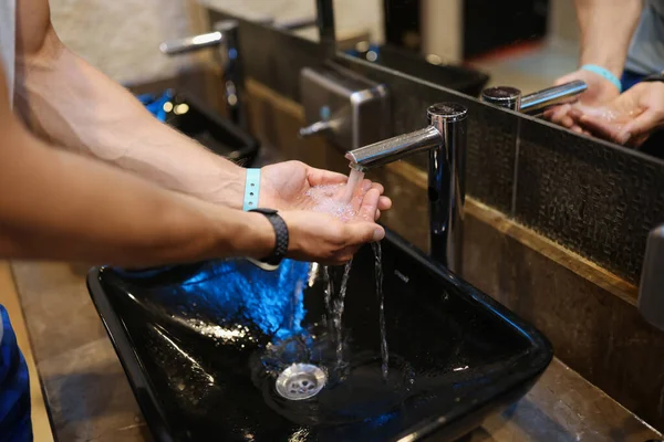 Uomo che si lava le mani sotto l'acqua corrente dal rubinetto in bagno pubblico primo piano — Foto Stock