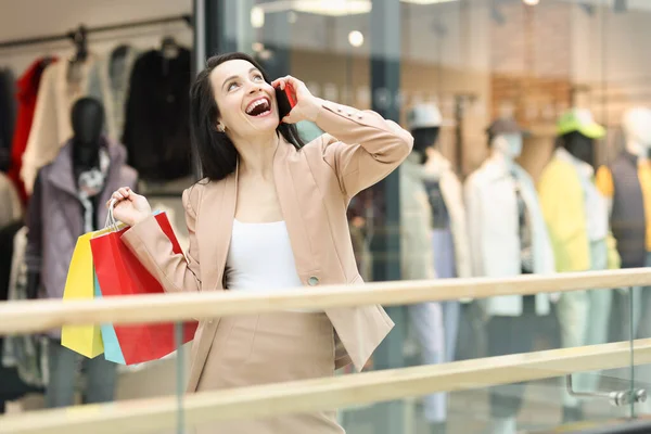 Jovem mulher feliz segurando muitos sacos de papel coloridos e falando no telefone na loja — Fotografia de Stock