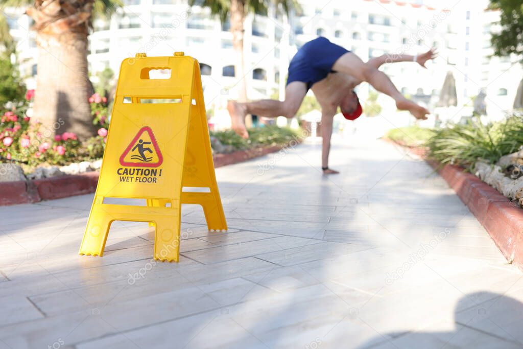 Yellow sign caution wet floor standing near falling man closeup