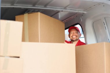 Gülümseyen erkek kurye arabadan karton kutu çıkarır.