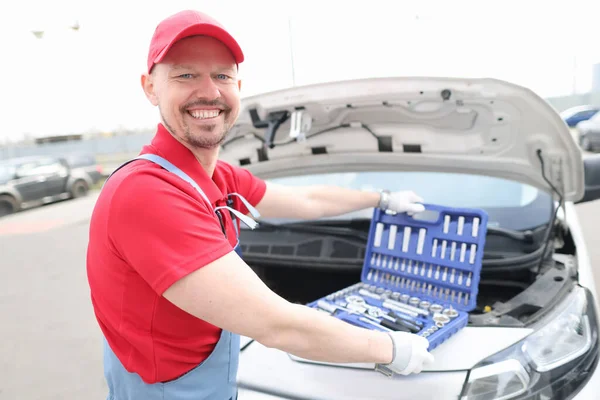 Retrato de jovem sorridente reparador de carro com conjunto de ferramentas no capô do carro — Fotografia de Stock