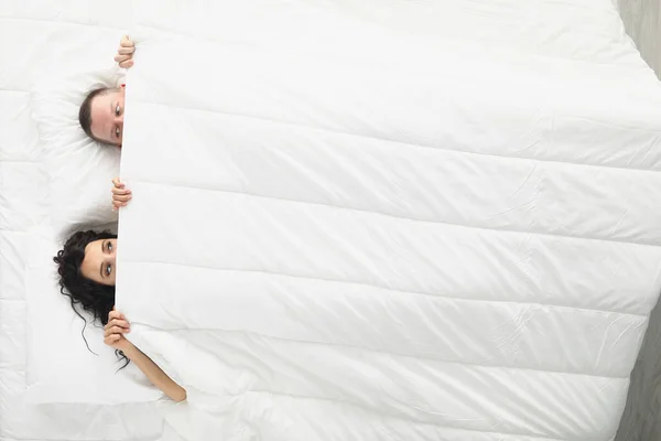Νεαρό παντρεμένο ζευγάρι ξαπλωμένο κάτω από κουβέρτα στο κρεβάτι με θέα — Φωτογραφία Αρχείου