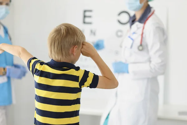 医生眼科医生戴着防护面罩在诊所检查小男孩的视力 — 图库照片