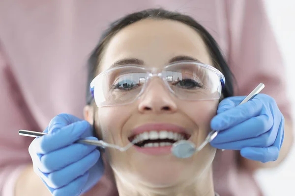 Dentysta badający jamę ustną pacjentki noszącej okulary ochronne w klinice — Zdjęcie stockowe