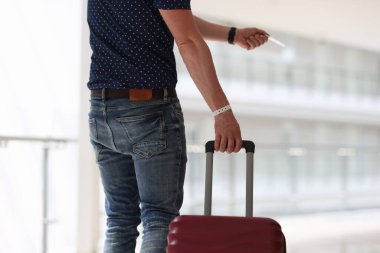 Elinde bavulu olan bir adam otel odasının plastik anahtarını tutuyor.