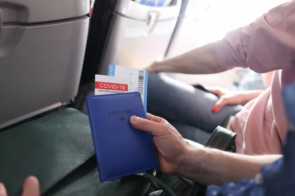 Hombre volando en avión y sosteniendo pasaporte de inmunización contra covid 19 y boletos de primer plano — Foto de Stock