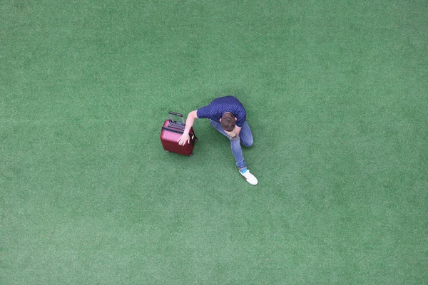 Triste hombre con la maleta sentada en la hierba verde y sosteniendo su cabeza vista superior — Foto de Stock