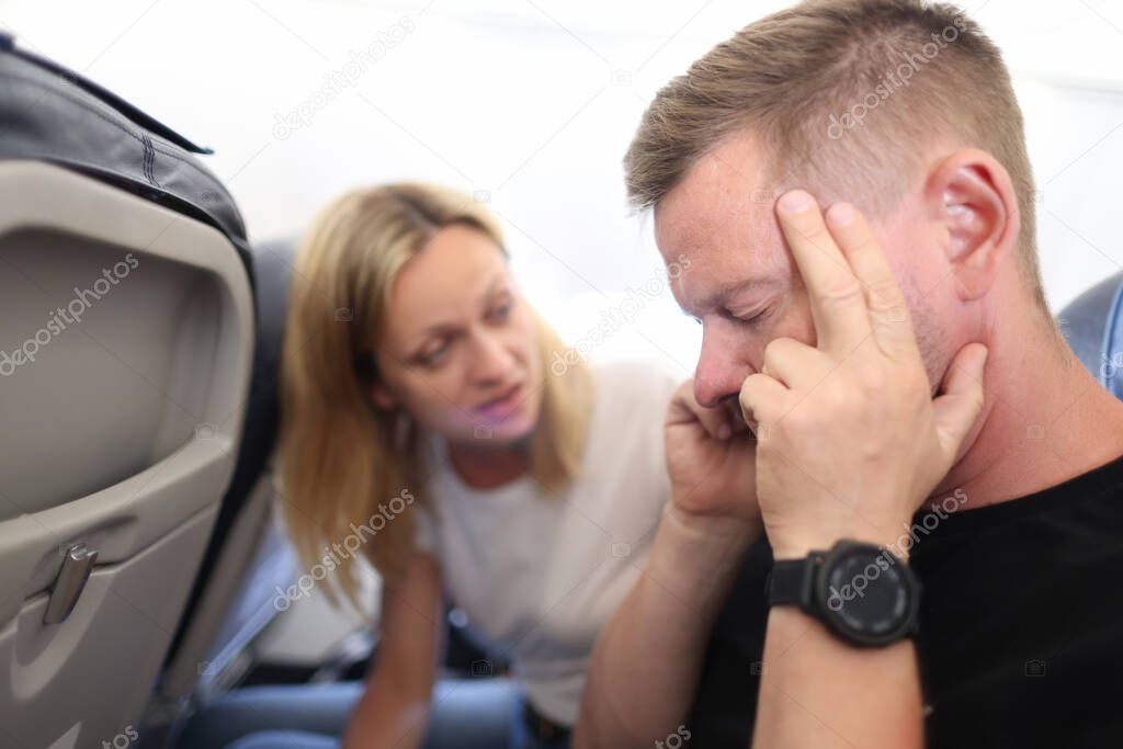 Young man is flying in airplane and holding sore head