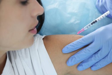 Hemşire klinikte genç bir kadının omzuna iğne yapıyor.