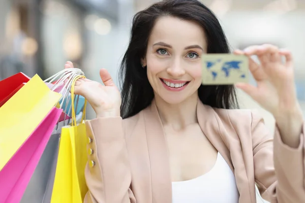 Egy fiatal, mosolygós nő portréja, kezében hitelkártyával és bevásárlószatyrokkal. — Stock Fotó