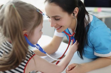 Doktor steteskopla küçük kızı dinliyor ve onunla klinikte oynuyor.