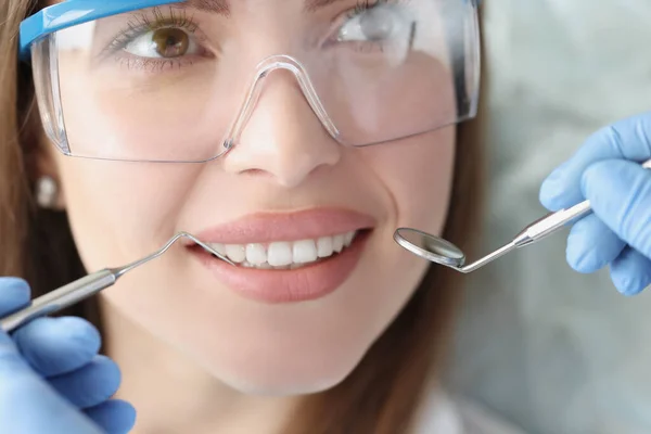 Dentista sosteniendo instrumentos dentales frente a la cara de la mujer — Foto de Stock