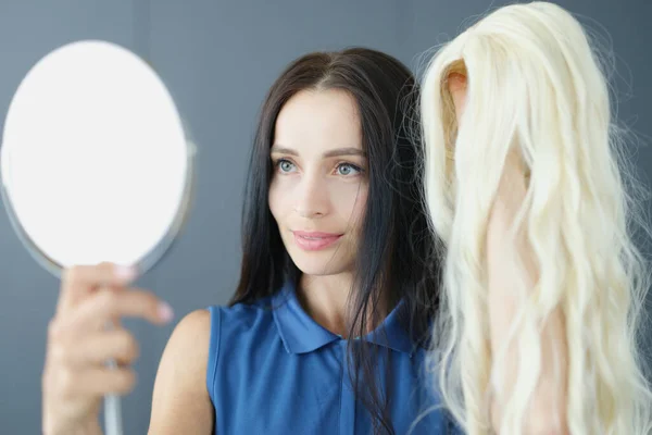 Mladá brunetka žena drží bílou paruku před zrcadlem — Stock fotografie