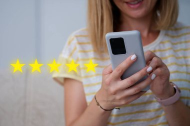Elinde cep telefonu tutan ve 5 yıldızlı hizmet notu veren bir kadın.