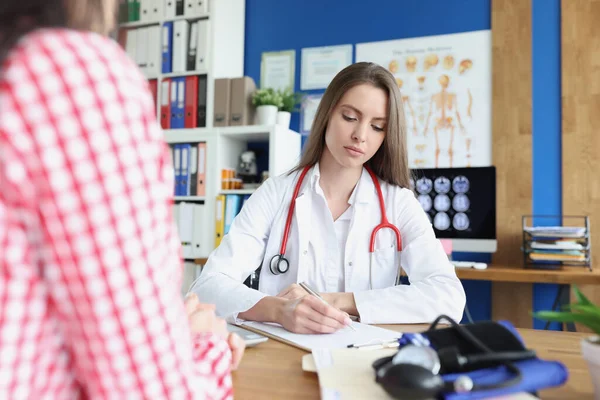 Médecin écrivant dans des documents à côté d'une patiente en clinique — Photo