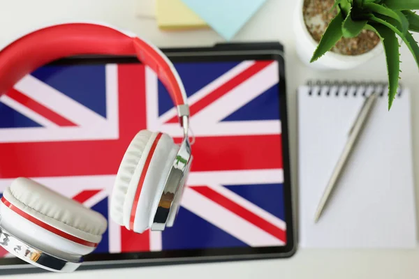 Tabletka z wizerunkiem brytyjskiej flagi ze słuchawkami i notatnik z długopisem leżą na stole — Zdjęcie stockowe