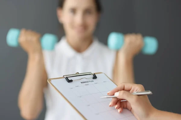 Treinador preenchendo plano de treino de esportes no fundo da mulher com halteres closeup — Fotografia de Stock