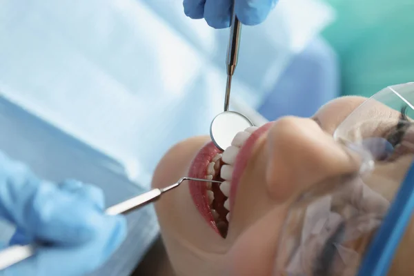Tandläkare i skyddshandskar undersöker tänder kvinnliga patienten med metallinstrument i kliniken närbild — Stockfoto