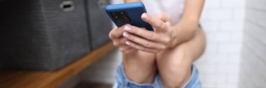 Kişi tuvalete oturur ve akıllı telefonu elinde tutar.