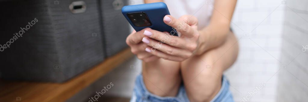 Person sits on toilet and holds smartphone in his hands