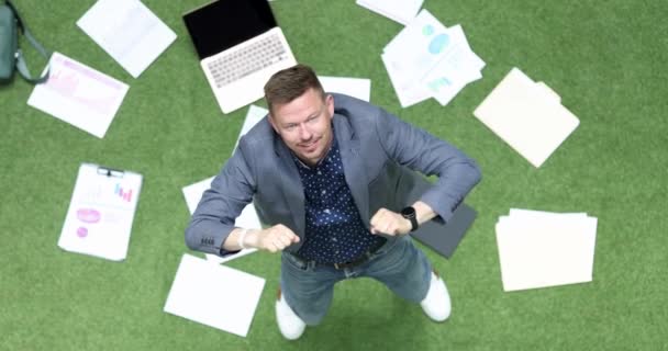 Businessman happily dances on green lawn, lies laptop and business charts 4k movie — Stok video