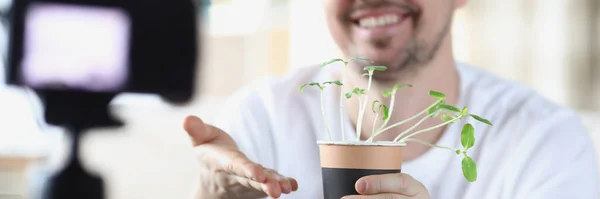 Lächelnder Mann demonstriert Keimlinge auf Videokamera — Stockfoto