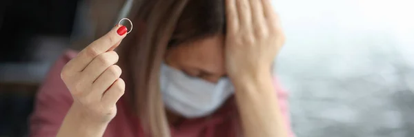 Mulher triste em máscara protetora segurando anel de casamento em sua mão — Fotografia de Stock