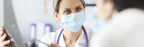 Dokter in beschermend masker toont patiënt X-ray — Stockfoto