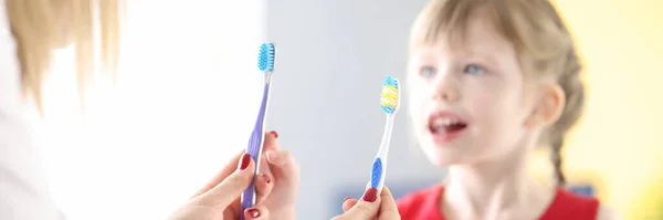 Médico segurando duas escovas de dentes na frente da menina — Fotografia de Stock