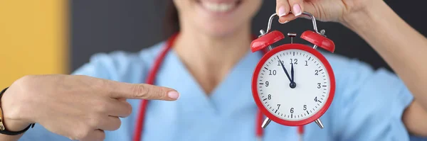 Smiling nurse points finger at red alarm clock