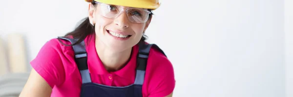 Lachende vrouwelijke bouwvakker in gele helm gebogen over blauwdrukken — Stockfoto