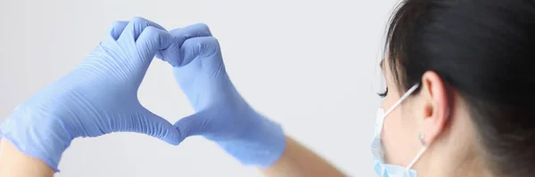 Dokter bertopeng pelindung medis dan sarung tangan memegang tangannya dalam bentuk hati. — Stok Foto