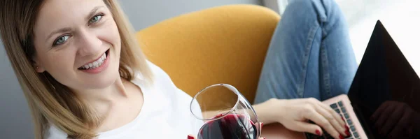 Femme avec un verre de vin assis avec un ordinateur portable sur ses genoux — Photo