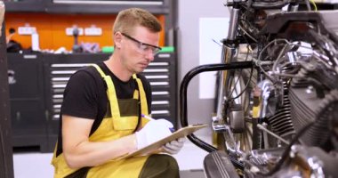 Erkek tamirci, servis merkezinde motosiklet parçalarını teşhis ediyor.