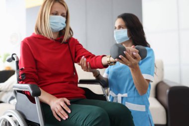 Tekerlekli sandalyedeki ve koruyucu maskeli bir kadın halterle egzersiz yapıyor.