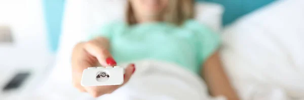 Жінка лежить в ліжку натискає кнопки на пульті дистанційного керування — стокове фото