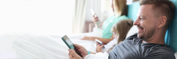 Батьки з дитиною лежать на ліжку зі смартфонами — стокове фото