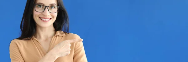 Frau in Brille zeigt Finger ins Leere auf blauem Hintergrund — Stockfoto
