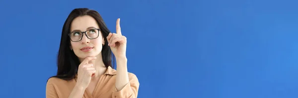 Pensive nő szemüvegben mutató ujj fel a kék háttér — Stock Fotó