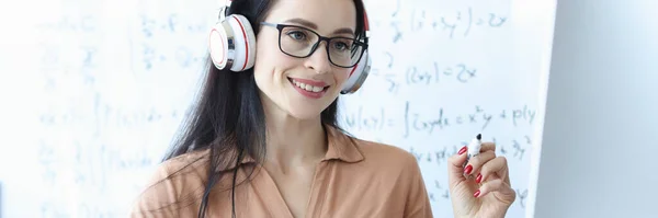 Guru perempuan di headphone melihat layar komputer di latar belakang papan tulis — Stok Foto