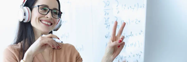Woman teacher in headphones showing two fingers in computer screen
