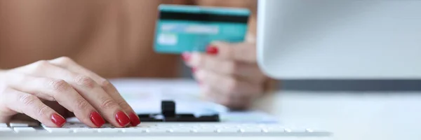 Woman typing on computer keyboard and holding bank card in her hands closeup