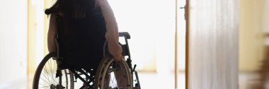 Tekerlekli sandalyedeki kadın karanlık koridorda pencereden dışarı bakıyor.
