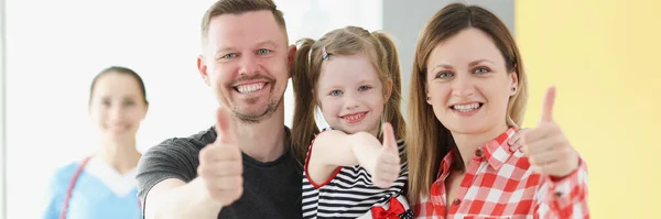 Glimlachende familie doet duimen omhoog gebaar in de achtergrond is arts — Stockfoto