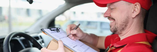 Smiling courier driver in car with documents and box — Stock Photo, Image