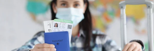 Kvinna i medicinsk skyddsmask och resväska visar hennes pass innehar pass immunitet mot coronavirus infektion — Stockfoto