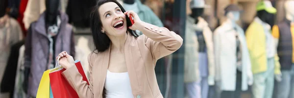 Vidám nő beszél okostelefonon, és tartsa bevásárló táskák a plázában — Stock Fotó