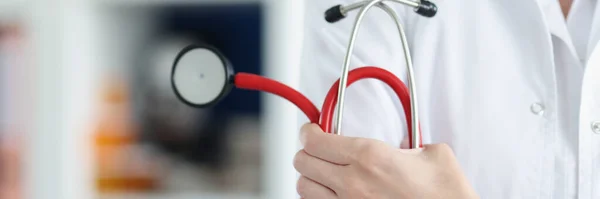 Médico segura estetoscópio vermelho com braços dobrados — Fotografia de Stock