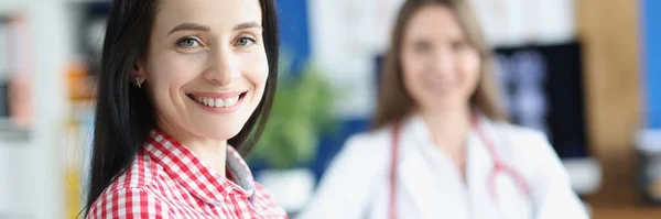 Lächelnde junge Patientin über Hintergrund des Arztes in Arztpraxis — Stockfoto