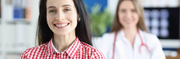 Tersenyum pasien wanita muda di latar belakang dokter di kantor medis — Stok Foto